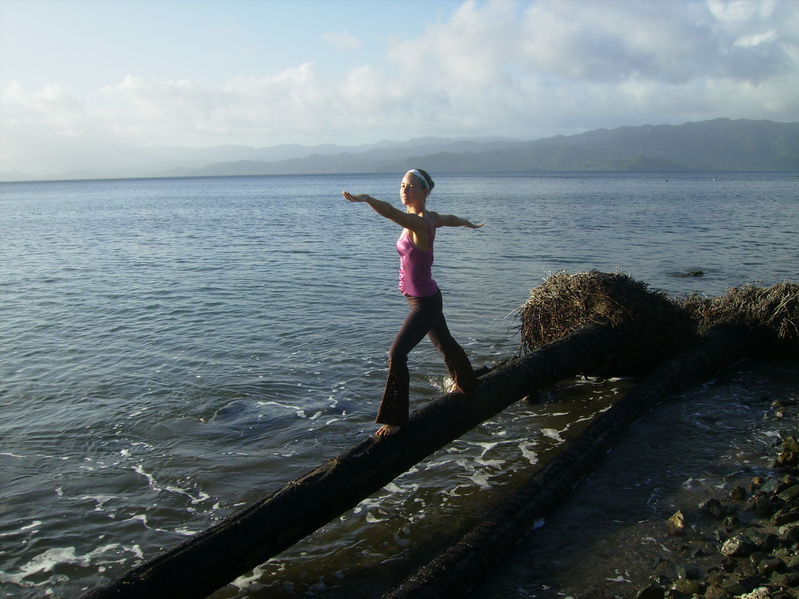 A woman practices yoga on a washed-up palm tree overlooking Savusavu bay